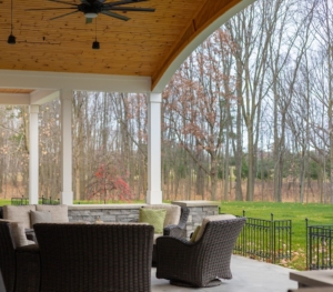 Covered patio with wicker chairs and wooded view at a Holland lake-access home.