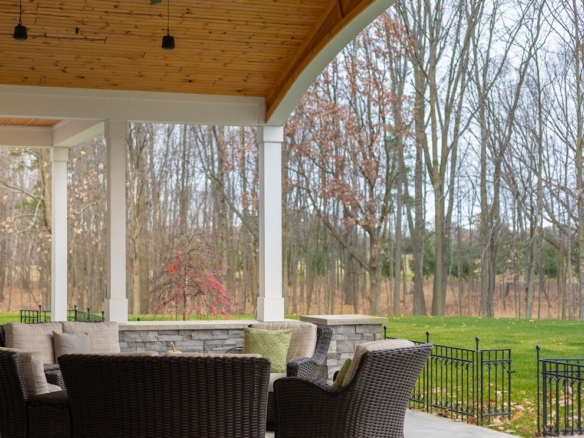 Covered patio with wicker chairs and wooded view at a Holland lake-access home.