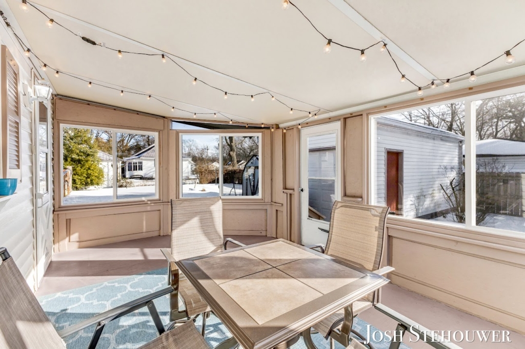 Bright four-season porch in a Grand Haven home with string lights, patio table, and winter views outside the windows.
